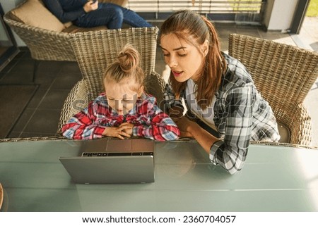 Calm mother helping her daughter to do homework while using laptop