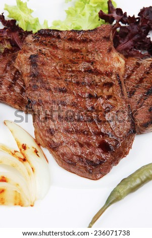 meat food : two grilled steak with chili and red peppers , green lettuce salad , on dish isolated over white background
