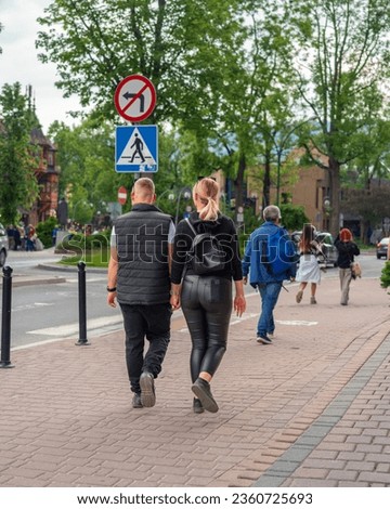 A young couple of lovers walks through the city, enjoying each other on a busy street. No parking sign and crossing sign in the background. Urban lifestyle for relationships and urban projects
