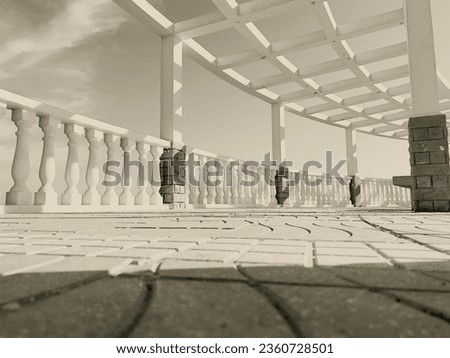 "A timeless black-and-white photograph captures the serene ocean view from a terrace adorned with a Greek-style pergola. The monochrome tones add a classic touch, evoking a sense of nostalgia and eleg