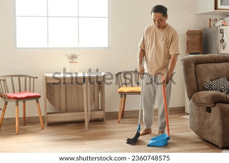 Man with broom sweeping floor at home Royalty-Free Stock Photo #2360748575