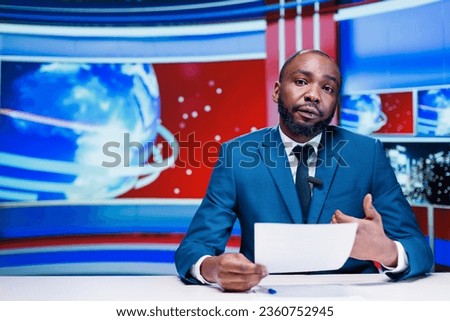 Presenter delivering news from papers headlines, reporting exclusive information about latest events worldwide. African american news anchor transmitting details about business or politics. Royalty-Free Stock Photo #2360752945
