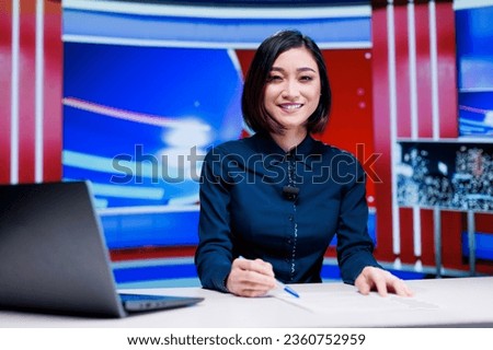 Asian presenter on daily newscast in newsroom, talking about latest international events on live broadcast. Woman reporter creating television content with media outlets headlines. Royalty-Free Stock Photo #2360752959