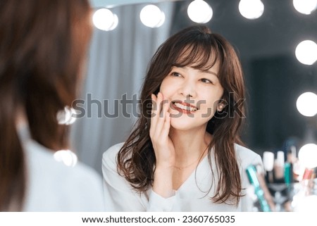 Asian middle-aged woman smiling while looking in the mirror. Cosmetics. Skin care. Royalty-Free Stock Photo #2360765035