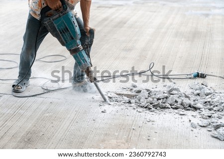 Worker at construction site demolishing concrete with electric jack hammer. Royalty-Free Stock Photo #2360792743