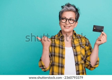 Photo of attractive retired woman credit card point look empty space wear trendy plaid yellow clothes isolated on cyan color background