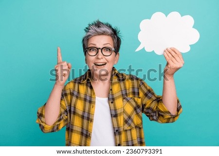 Photo portrait of lovely senior lady hold paper cloud finger point up wear trendy plaid yellow garment isolated on cyan color background