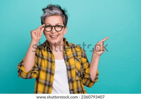 Photo portrait of charming grandmother touch specs point empty space wear trendy plaid yellow outfit isolated on cyan color background
