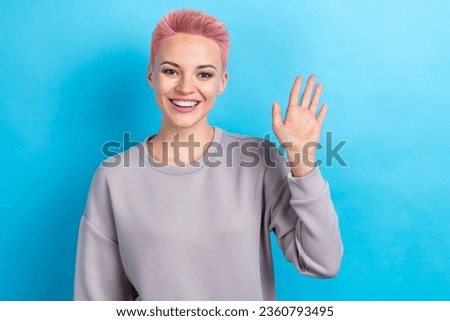Photo of good mood pretty woman with dyed hairstyle dressed gray sweatshirt vawing arm to you say hi isolated on blue color background