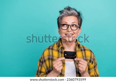 Photo portrait of charming grandmother credit card look empty space wear trendy plaid yellow outfit isolated on cyan color background