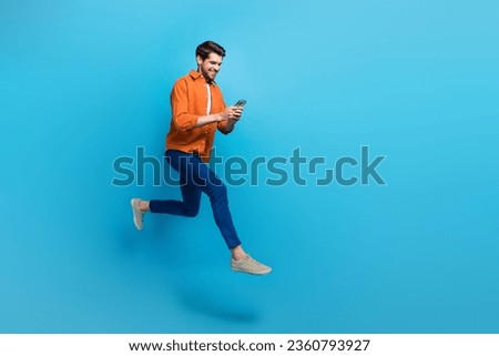 Full size profile photo of energetic attractive man use smart phone jumping run hurry empty space ad isolated on blue color background