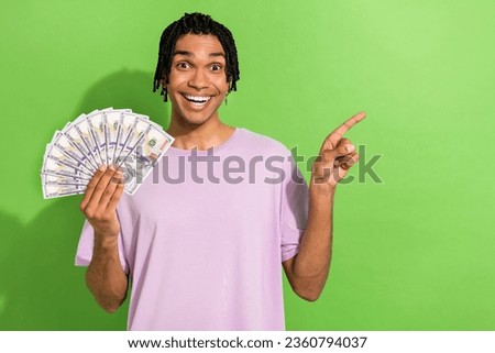 Photo of astonished handsome guy hold dollar bills indicate finger empty space ad isolated on green color background