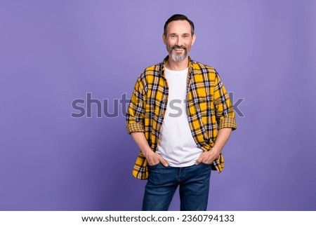 Portrait of optimistic person with gray beard dressed checkered shirt hold hands in pockets smiling isolated on violet color background