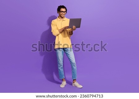 Full body length photo of optimistic young businessman wear yellow shirt denim jeans elearning courses isolated on violet color background
