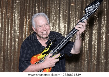Photo Booth. A man smiles and poses like a Rock Star with an Inflatable Guitar while waiting to have his pictures taken in a Photo Booth at a Wedding Party. Photo Booth Props. Guitar. Rock Star. FUN. 