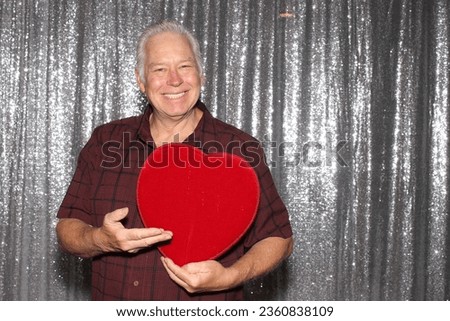 Photo Booth. Valentines Day. A man smiles and poses with a Red Heart Shaped Box of Assorted Chocolates while having his picture taken in a Photo Booth. Photo Boots are perfect for Valentines day. 
