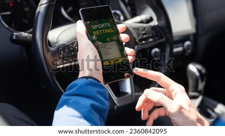 Close up cropped shot of man hand holding mobile phone with bookmaker;s website on its screen. Male gambler betting online using mobile application white sitting in a car.