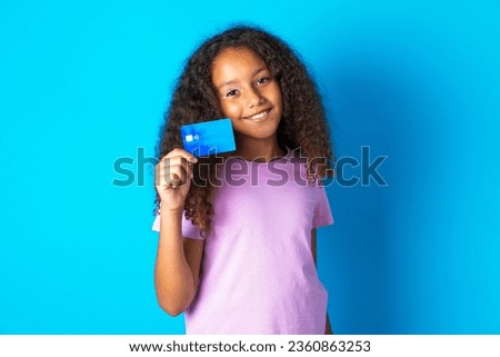 Close up photo of optimistic beautiful kid girl with afro curly hairstyle wearing pink T-shirt hold card