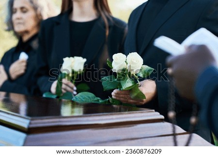 Focus on two fresh white roses held by mourning man in black suit during funeral service while standing by coffin against his daughter and wife Royalty-Free Stock Photo #2360876209