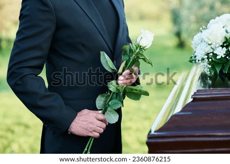 Cropped shot of mature widower in black suit holding fresh white roses while standing by coffin with dead body of his wife at funeral Royalty-Free Stock Photo #2360876215