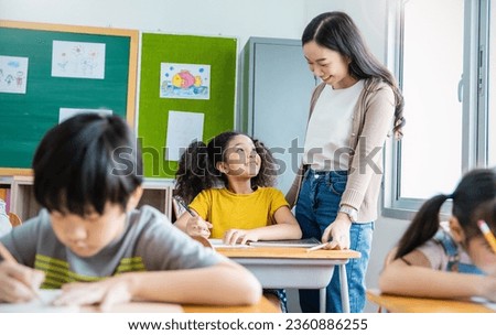 Pupil black girl with teacher in classroom at elementary school. Student girl studying in primary school. Children writing notes in classroom. Education knowledge, successful teamwork concept banner Royalty-Free Stock Photo #2360886255