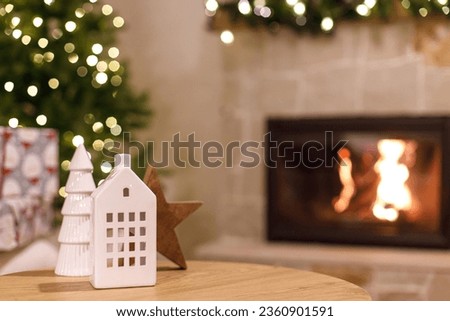Atmospheric christmas time. Stylish white house and tree decor in festive room, christmas eve time. Christmas modern decoration on table against burning fireplace.