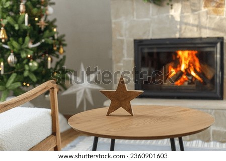 Christmas modern decoration on table against burning fireplace. Stylish wooden star decor in festive room, christmas eve time. Atmospheric christmas time.