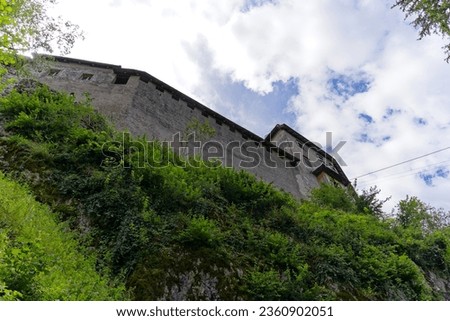Looking up stone wall and tower of castle on a rock at Slovenian City of Bled on a blue cloudy summer day. Photo taken August 8th, 2023, Bled, Slovenia.