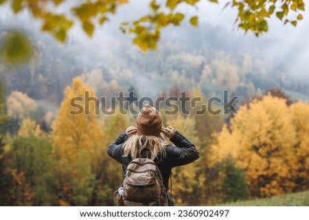 Autumn hiking. Woman puts on knitted hat during hike in mountains forest in cold foggy weather Royalty-Free Stock Photo #2360902497