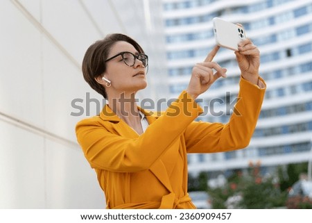 Smiling  beautiful  woman with short haircut  in yellow jacket and pants using mobyle phone. Standing over modern city. Outdoor photo.