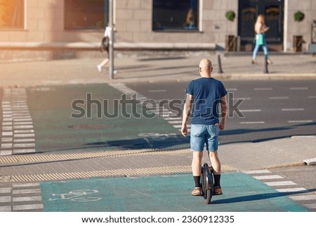 Man rides on electric mono wheel, crossing road, ride on separate lane for cyclist. Man cycling on monowheel. Boy travel on monowheel. Electric unicycle (EUC), personal mobility.  Royalty-Free Stock Photo #2360912335