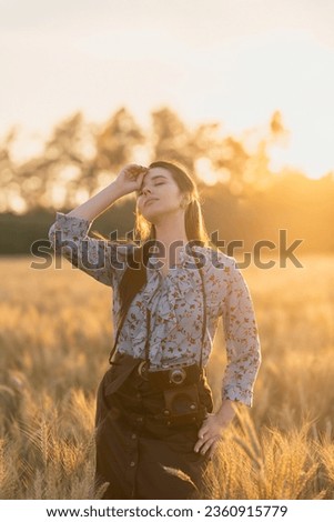 Girl with a retro photo camera in a golden rye field at sunset