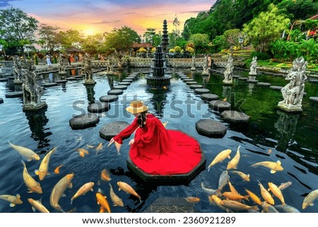 Woman feeding colorful fish in pond at Tirta Gangga Water Palace in Bali, Indonesia. Royalty-Free Stock Photo #2360921289