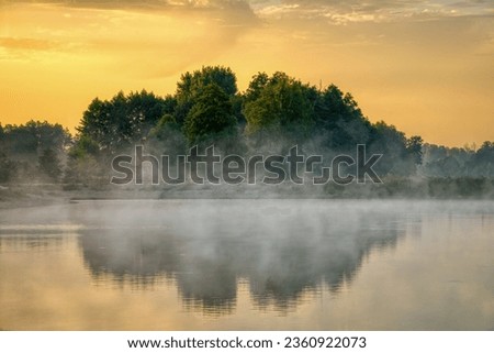 Scenic view of a country lake landscape with trees reflected in the water and fog. Morning of the beginning of autumn.