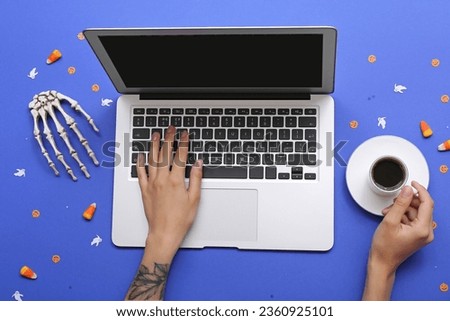 Female hands with laptop, cup of coffee and Halloween decorations on blue background