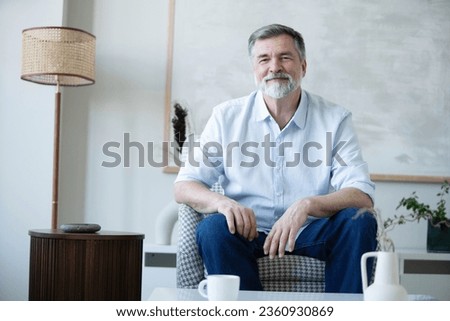 Portrait of happy mature man sitting on sofa at home. Royalty-Free Stock Photo #2360930869