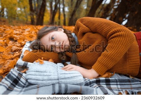 a young teenage girl is lying in a glade by the river bank in an autumn forest, enjoying the beautiful nature and bright yellow leaves