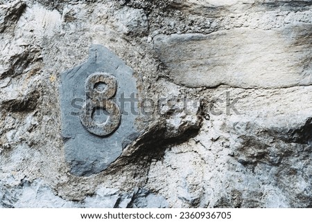 Natural stone slate street sign with number eight - Sign on the wall of a house indicating the postal address number