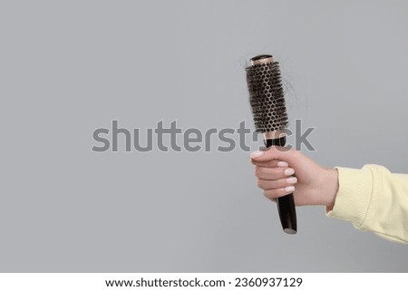 Woman holding brush with lost hair on grey background, closeup and space for text. Alopecia problem