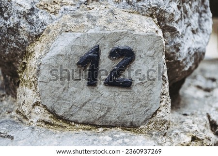 Natural stone slate street sign with number twelve - Sign on the wall of a house indicating the postal address number