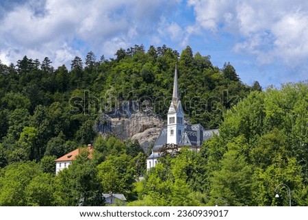 Scenic view of white Saint Matin church at lakeshore of Lake Bled on a cloudy summer day. Photo taken August 8th, 2023, Bled, Slovenia.