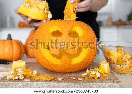 Woman gutting Halloween pumpkin. Female hollowing Jack-o'-lantern, removing guts and seeds from a Halloween pumpkin by reaching inside through the cut-off top lid.