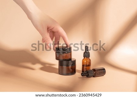 Female hand touching unbranded amber glass jar with face mousturizing cream. Bottle for professional cosmetics product. Skincare and beauty concept. Mockup Royalty-Free Stock Photo #2360945429