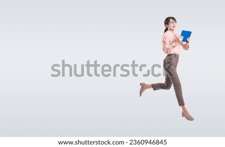 Asian middle-aged business woman wearing a suit using a tablet PC while jumping energetically Royalty-Free Stock Photo #2360946845