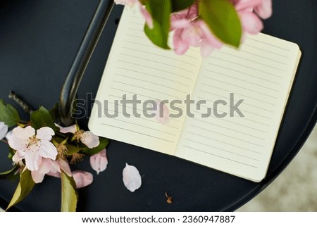 Open notebook and flowers and on the small black table on terrace at home in a sunny day, outdoor workspace, summer relaxation, notes, ideas, planning
