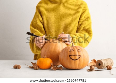 Woman painting pumpkin for Halloween celebration on light background Royalty-Free Stock Photo #2360949781