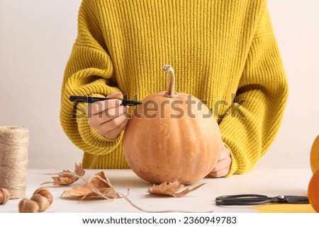 Woman painting pumpkin for Halloween celebration on light background Royalty-Free Stock Photo #2360949783