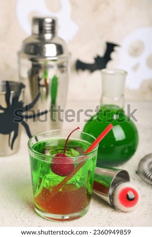 Glass of delicious cocktail for Halloween with tasty cherry, measure cup and candy on light background, closeup