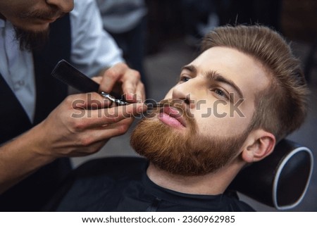 Handsome bearded man is getting shaved by hairdresser at the barbershop Royalty-Free Stock Photo #2360962985