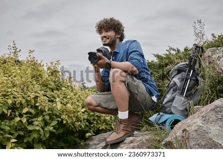 travel photographer concept, happy indian man taking photo on camera in natural place, banner